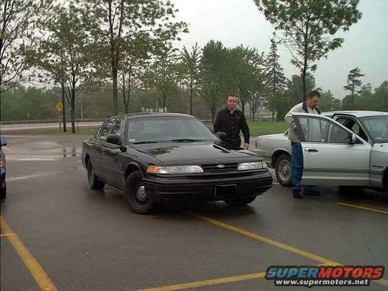 Black 2000 Ford Crown Victoria parked on wet asphalt, with a silver car to its right