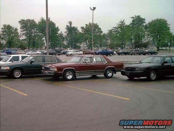 Maroon sedan parked in a lot next to a black sedan. Trees and other cars in background