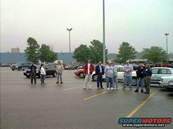 Group of people gathered in a parking lot with several cars visible