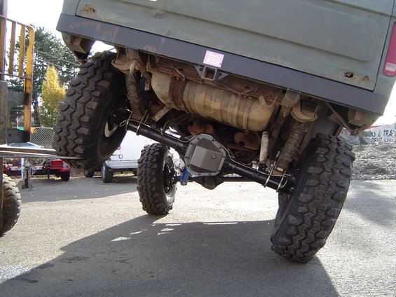 Rear axle and suspension of a lifted vehicle with large tires. A pink sticker is visible on the frame