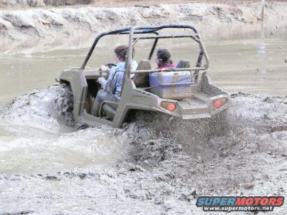 Gray UTV driving through mud, rear view