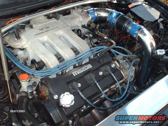 Close-up of a Mazda V6 engine with DOHC 24-valve labeling on the intake manifold and blue spark plug wires