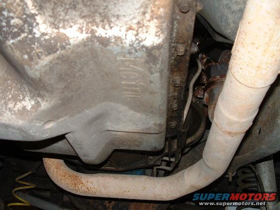 Underside of a vehicle showing a rusty exhaust pipe and a dirty transmission pan with faint markings