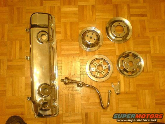 Chrome valve cover and four hubcaps on wooden floor