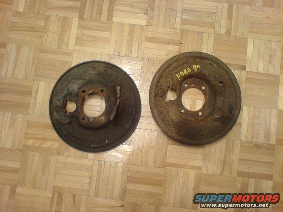 two rusty brake drums on a wood floor, one has 'FORD 9"' written on it