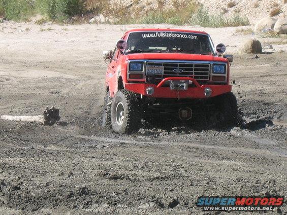 Red 1987 Ford Bronco with winch driving through mud