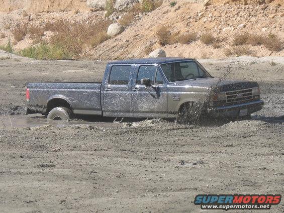 Side view of a muddy 1987 Ford F-Series pickup truck stuck in mud
