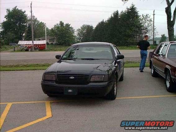 Black 2000 Ford Crown Victoria parked, another car to the right, person walking away