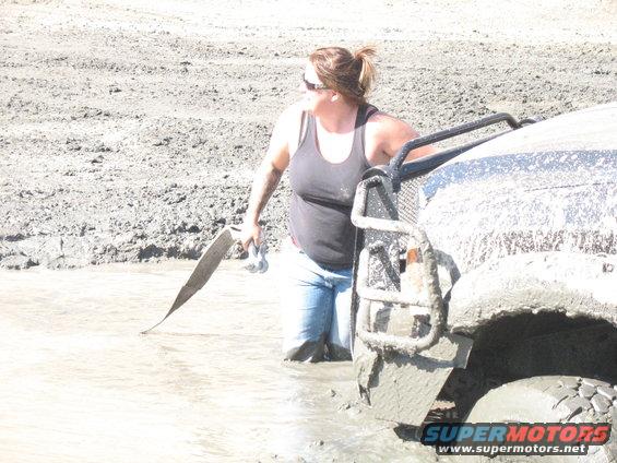 Mud-covered vehicle front corner with woman in water holding tow strap