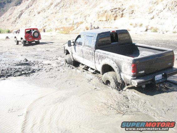 Black pickup truck stuck in mud with a red SUV behind it