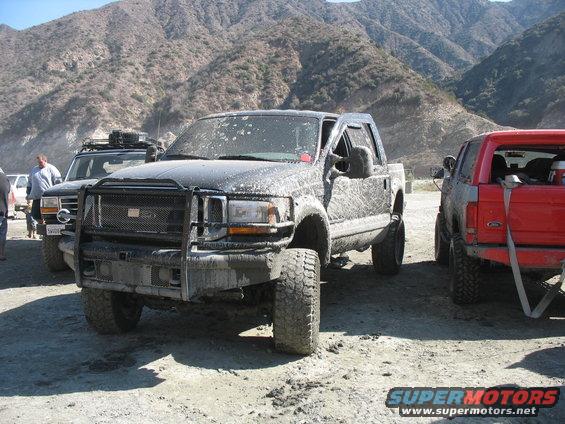 Black Ford F-250 truck covered in mud, with a large grille guard and lifted suspension