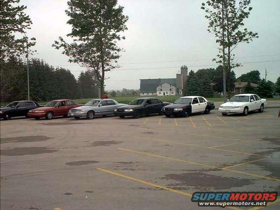 Six Ford Crown Victorias parked in a lot, some are police cars