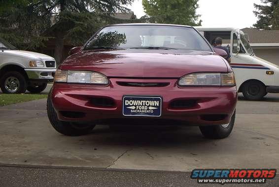 Red sedan with a 'Downtown Ford Sacramento' plate. White truck in background