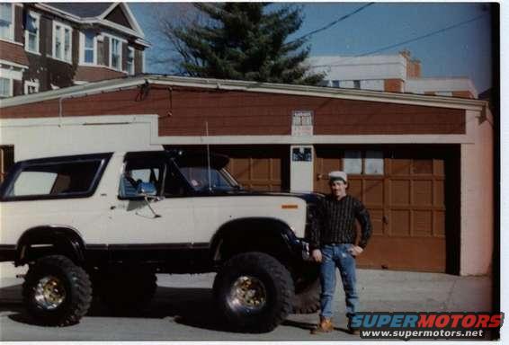 White and black 1980 Ford Bronco parked in front of a garage with a man standing beside it
