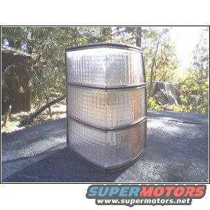 Clear plastic tail light assembly with three stacked sections, resting on a dark surface outdoors