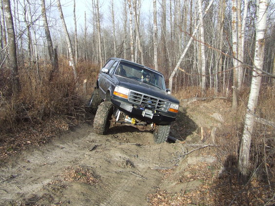 Black Ford Bronco with lifted suspension driving on a dirt trail through trees