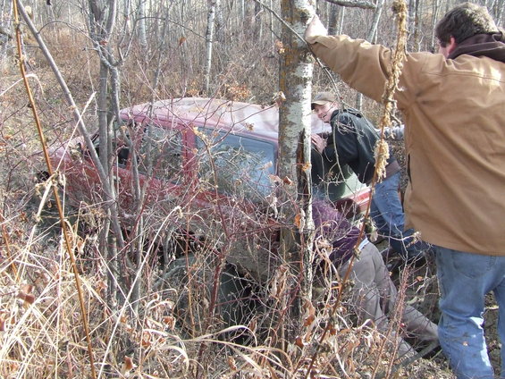 Side view of a red vehicle stuck in brush with people around it