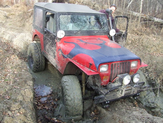 Red Jeep Wrangler with blue flames on hood stuck in a muddy ditch. Snorkel visible