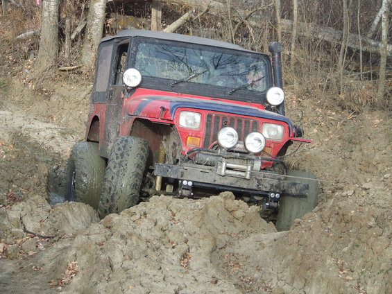 Red Jeep Wrangler with snorkel and winch stuck deep in mud on a wooded trail