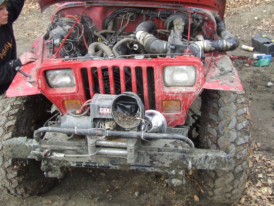 Red Jeep Wrangler, hood open, showing engine. Has a winch on front bumper. Muddy tires and body