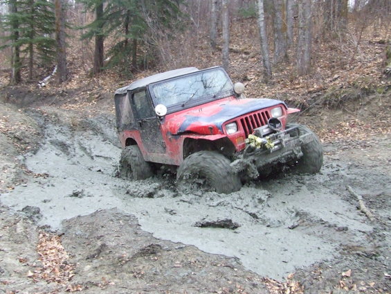 Red Jeep Wrangler stuck deep in mud on a wooded trail