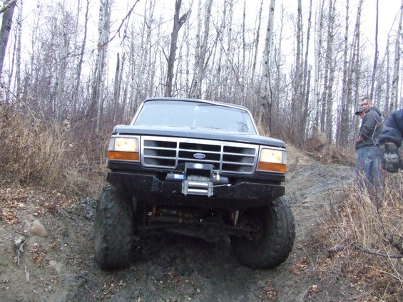 Black Ford Bronco with a winch on the front bumper, angled uphill on a muddy trail