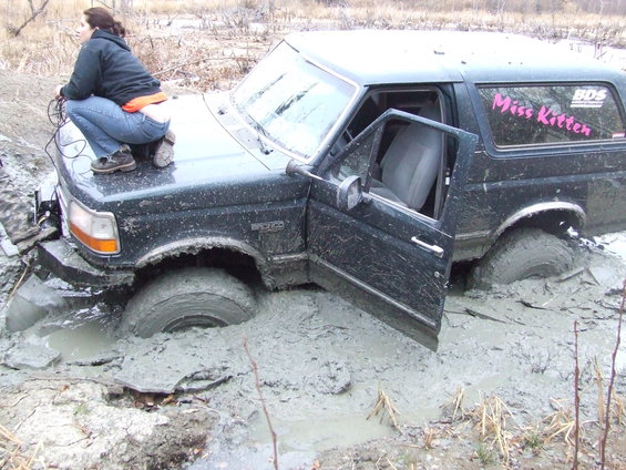 1990 Ford Bronco stuck in mud with driver's door open. 'Miss Kitten' sticker on rear window