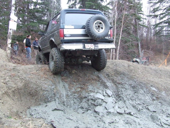 1990 Ford Bronco climbing a muddy incline, spare tire mounted on rear door