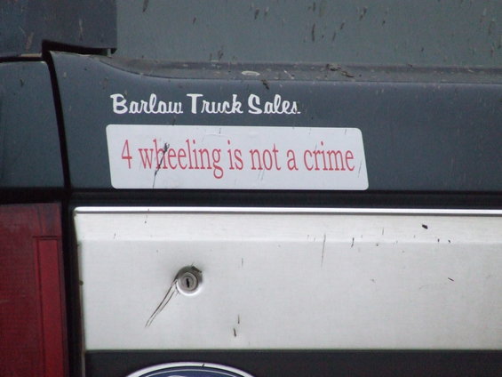 Rear gate of a vehicle with a 'Barlow Truck Sales' sticker and a '4 wheeling is not a crime' sticker