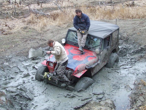 Red Jeep Wrangler stuck deep in mud with two men trying to free it