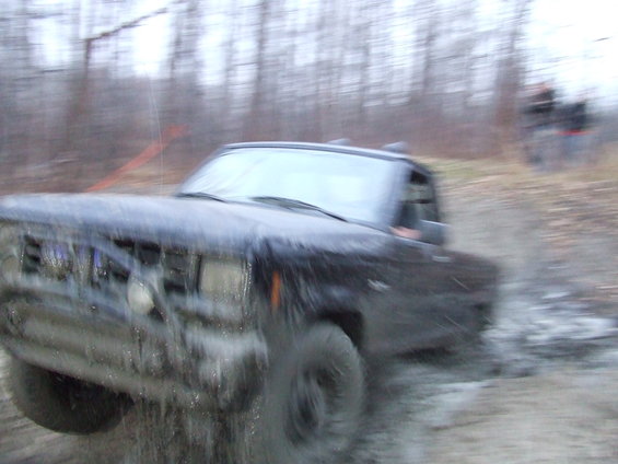 Black off-road vehicle splashing through mud, front view