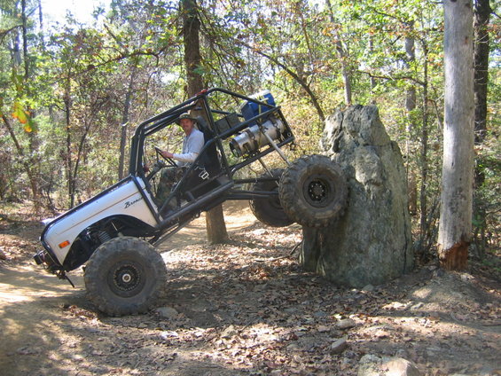 Off-road buggy with roll cage climbing a large rock on a dirt trail