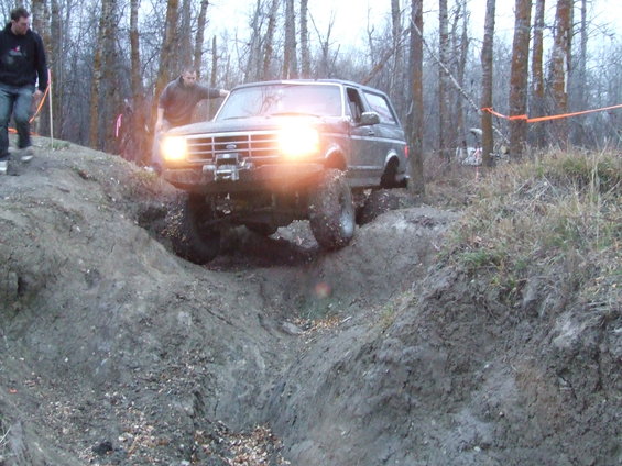 Ford Bronco climbing a muddy hill with two people nearby