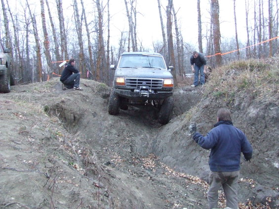 Ford Bronco navigating a muddy ditch with people watching