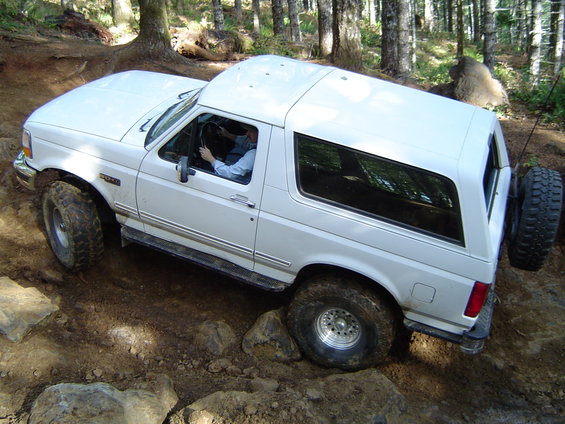 White Ford Bronco navigating rocky terrain in a forest