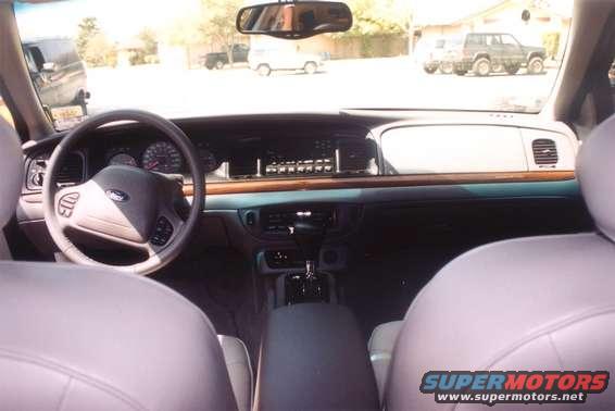 Interior view of a 2002 Ford Crown Victoria, showing the dashboard, steering wheel, and front seats. Other vehicles are visible outside