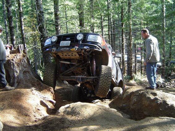 Off-road vehicle with large tires climbing over rocks on a wooded trail