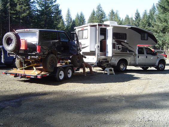 Black SUV on a trailer, being worked on next to a truck camper