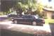 2002 Ford Crown Victoria - A dark sedan is parked in a driveway on a sunny day, with a house and trees in the background.