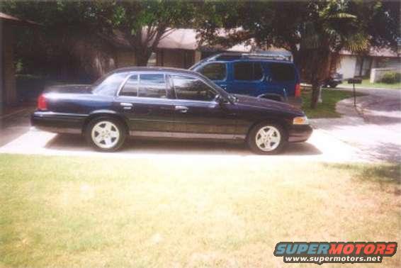 Dark sedan parked in driveway next to a blue SUV. It looks like a 2002 Ford Crown Victoria