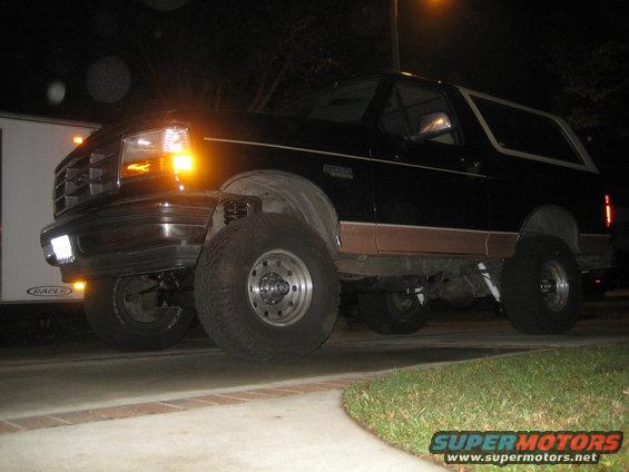 Black Ford Bronco with lifted suspension and aftermarket wheels, viewed from the front-right at night
