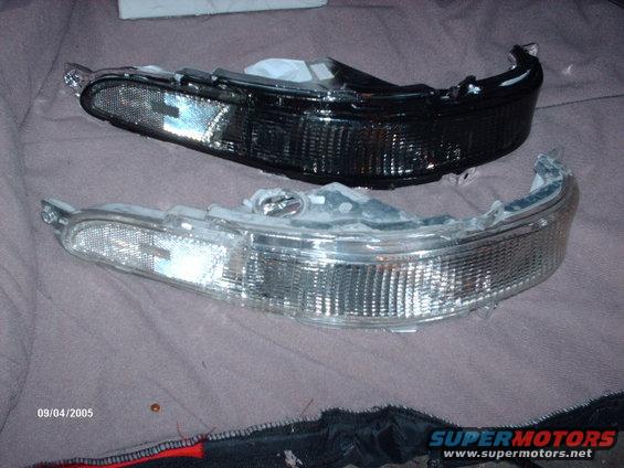 Two car headlights, one clear and one blacked out, lie on a textured surface