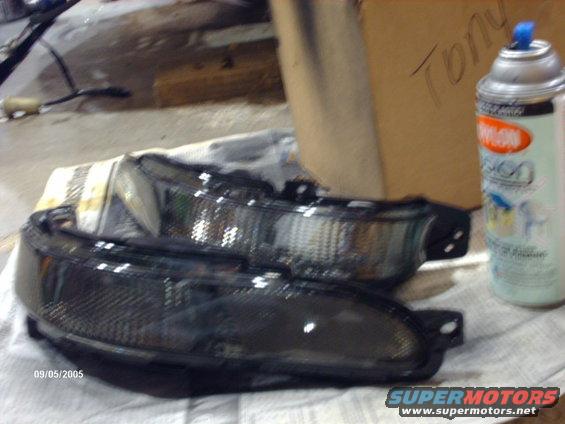 Two dark aftermarket headlights on a cloth, next to a spray can