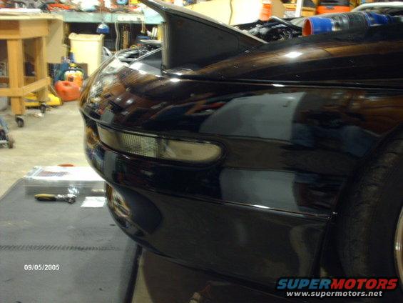 black sports car, front corner and fender visible, in garage with tools and equipment