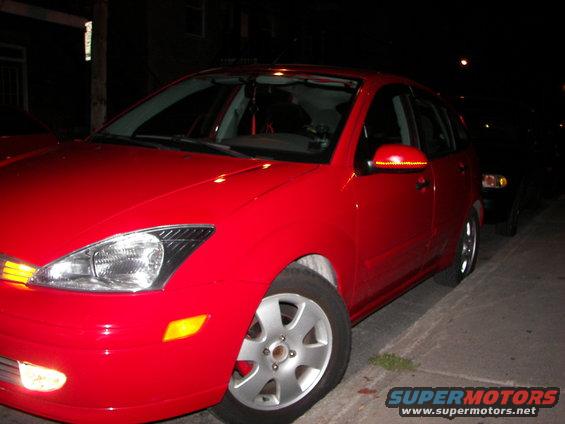 Red hatchback parked on street at night. Another car is visible behind it