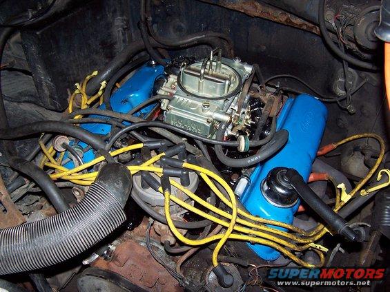 Close-up of a V8 engine with a Holley carburetor, blue valve covers, and yellow spark plug wires