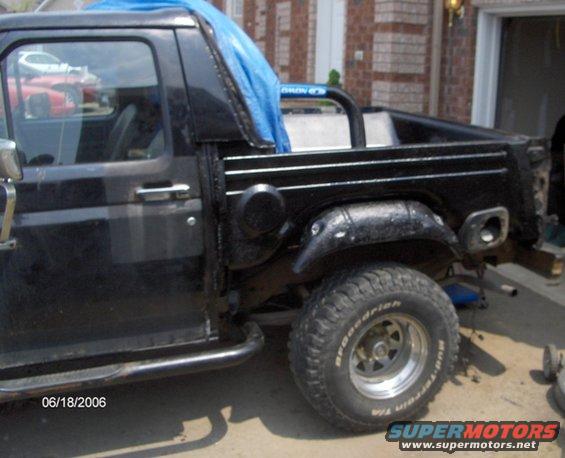 Black Ford Bronco, side view, showing rear quarter panel removed and blue tarp covering part of the interior