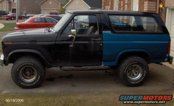 Side view of a black and blue Ford Bronco with aftermarket wheels and tires. The front fender is black, and the rear quarter panel is blue