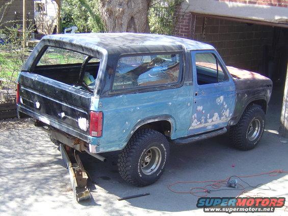 1986 Ford Bronco with primer and blue paint, rear bumper removed, parked in driveway