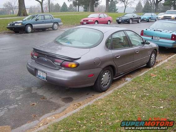 Gray Ford Taurus parked on street, rear view. Other cars visible